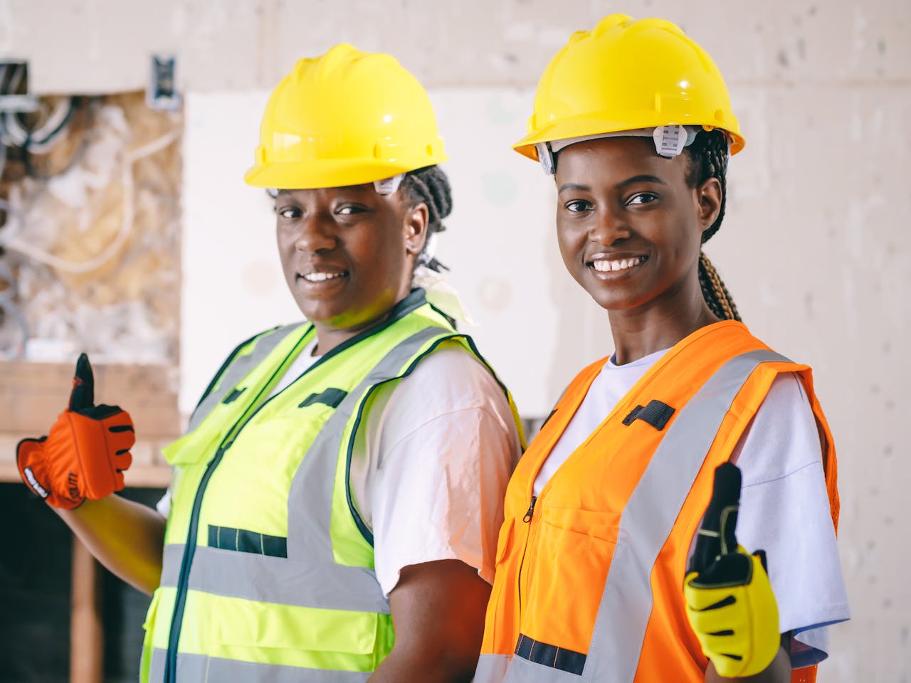 Two female construction workers wearing PPE, smiling and giving a thumbs up on site.